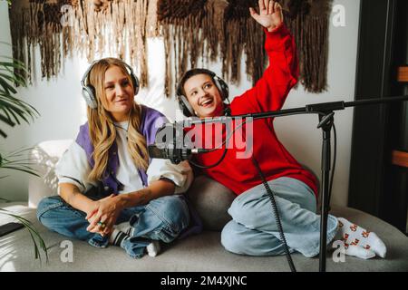 Glücklicher Musiker mit Kollegen, die Kopfhörer vor dem Mikrofon im Studio tragen Stockfoto