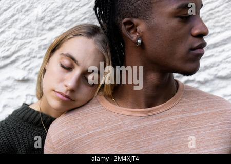 Eine Frau, die ihren Kopf vor der Wand auf die Schulter ihres Freundes legt Stockfoto