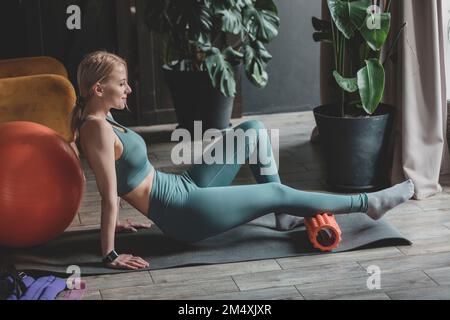 Lächelnde Frau mit Schaumstoffwalze auf der Trainingsmatte zu Hause Stockfoto