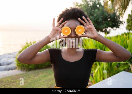 Glückliche Frau, die Orangenscheiben vor den Augen hält Stockfoto