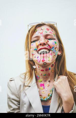 Glückliche Frau mit mehrfarbigen Aufklebern auf dem Gesicht vor weißem Hintergrund Stockfoto