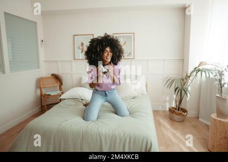Frau mit kabellosen Kopfhörern lacht auf dem Bett Stockfoto
