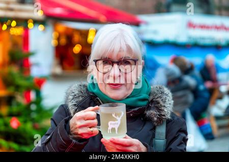 Lächelnde Seniorin mit einer Tasse Glühwein auf dem Weihnachtsmarkt Stockfoto