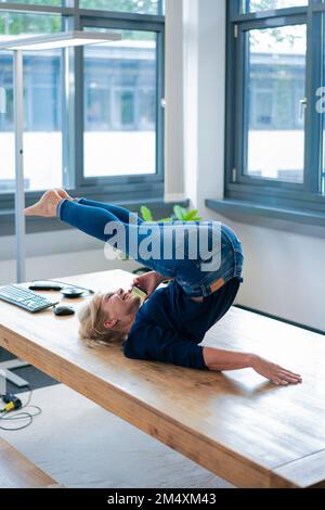 Glückliche Geschäftsfrau, die Yoga macht und am Schreibtisch telefoniert Stockfoto