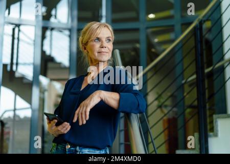 Eine nachdenkliche Geschäftsfrau, die ein Handy auf der Treppe hält Stockfoto