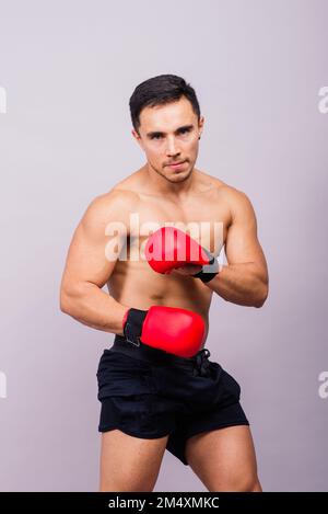 Muskulärer Modellsportler junger Mann in Boxhandschuhen auf grauem Hintergrund. Ein Mann, der seine Muskeln beugt. Stockfoto