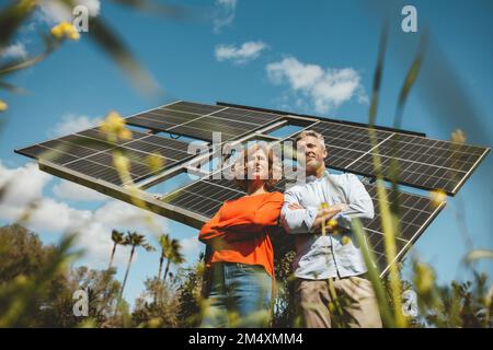 Reifes Paar mit gekreuzten Armen, das vor Solarpaneelen steht Stockfoto