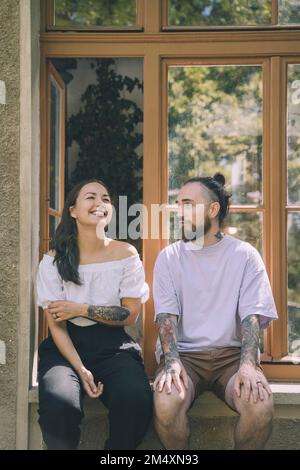Frau und Hipster sitzen auf dem Fensterbrett und reden miteinander Stockfoto