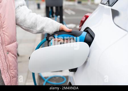 Frau, die das Ladegerät im Auto an der Station anschließt Stockfoto