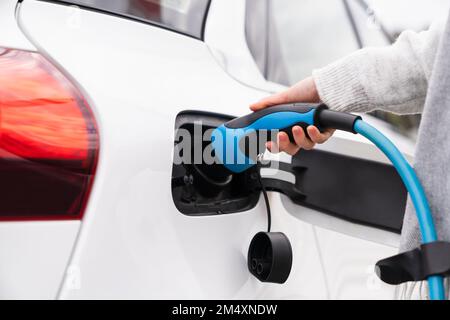 Eine Frau, die ein Ladegerät in einem Elektroauto an der Station anschließt Stockfoto