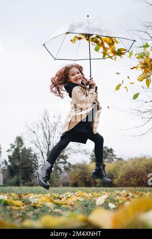 Fröhliches, süßes Mädchen, das im Park mit einem Regenschirm springt Stockfoto