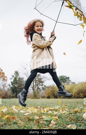 Fröhliches Mädchen, das im Park mit einem Regenschirm springt Stockfoto