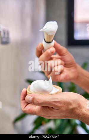 Hände eines Mannes mit Rasiercreme und Bürste im Badezimmer zu Hause Stockfoto