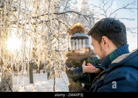 Glücklicher Mann, der seinen Sohn im Winterpark hält Stockfoto