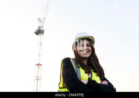 Glückliche Ingenieurin mit verschränkten Armen unter klarem Himmel Stockfoto