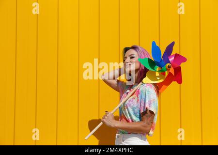 Lächelnde Frau, die an sonnigen Tagen ein farbenfrohes Spielzeug vor der gelben Wand hält Stockfoto