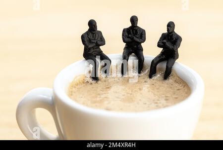 Eine Gruppe von Geschäftsmann-Figuren, die an einer Kaffeetasse sitzen und miteinander reden. Teamarbeit, Brainstorming-Konzept Stockfoto