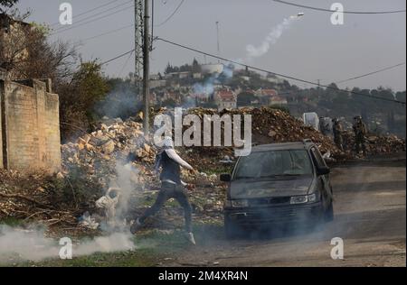 Nablus, Palästina. 23. Dezember 2022. Ein palästinensischer Protestteilnehmer wirft während der Zusammenstöße nach einem Protest gegen die Ausweitung jüdischer Siedlungen im Dorf Kufr Qadoom im Westjordanland in der Nähe von Nablus am 23. Dezember 2022 einen Tränengaskanister an israelische Soldaten zurück. Kredit: Nidal Eshtayeh/Xinhua/Alamy Live News Stockfoto