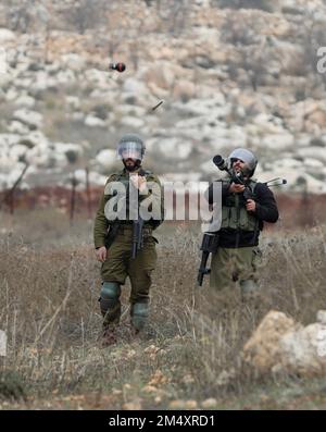 Nablus, Palästina. 23. Dezember 2022. Ein israelischer Soldat feuert während der Zusammenstöße nach einem Protest gegen die Ausweitung jüdischer Siedlungen im Dorf Beit Dajan östlich von Nablus am 23. Dezember 2022 einen Tränengaskanister auf palästinensische Demonstranten ab. Kredit: Ayman Nobani/Xinhua/Alamy Live News Stockfoto