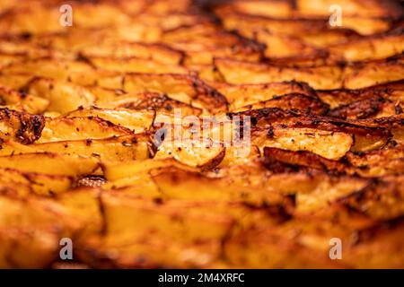 Beschreibung: Knusprige, goldbraune, gebackene Kartoffelkeile mit Paprika, Knoblauch, Salz, Pfeffer, Rosmarin, basilikum auf dem Tablett im Ofen, fotografiert von Stockfoto