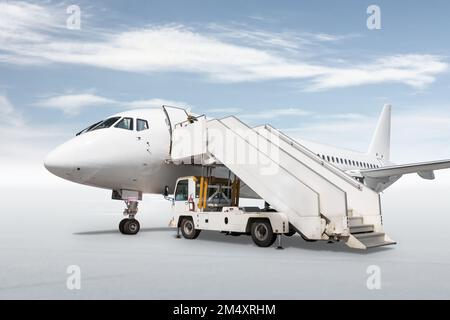 Weißes Passagierflugzeug mit einer Treppe, isoliert auf hellem Hintergrund mit Himmel Stockfoto