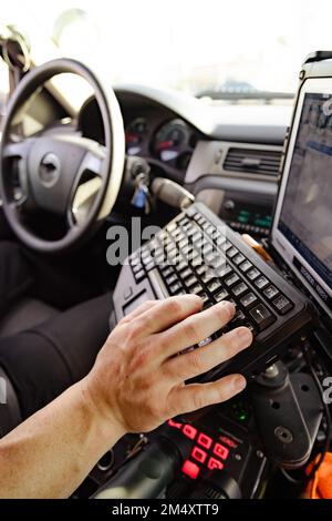 Weißer Polizist Hand und Finger, die in einem Polizeifahrzeug auf der Tastatur tippen und nach Informationen suchen, um besser fundierte Entscheidungen zu treffen, um zu ziehen Stockfoto