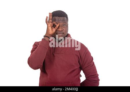 Junger selbstbewusster Mann, der mit der Hand und mit den Fingern eine gute Geste auf die Augen macht. Stockfoto