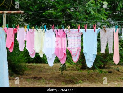 Kindersachen hängen an einem Seil im Hof des Hauses. Die Kleidung für das Baby wird auf der Straße auf Wäscheklammern getrocknet. Dinge eines Neugeborenen in di Stockfoto