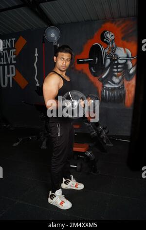 Ein vertikales Bild des südasiatischen Mannes, der Bizeps im Fitnessstudio hebt Stockfoto