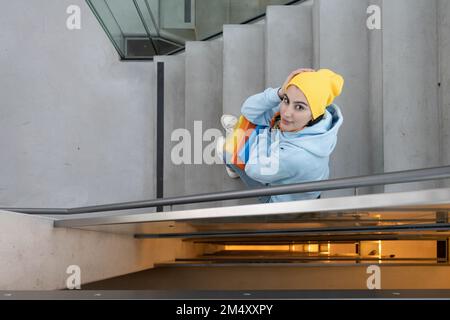 Ein Mädchen mit farbigen Ordnern in der Hand sitzt auf einer Steintreppe zwischen den Stockwerken und schaut nach oben Stockfoto