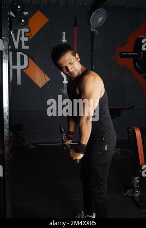 Ein vertikales Bild des südasiatischen Mannes, der Bizeps im Fitnessstudio macht Stockfoto