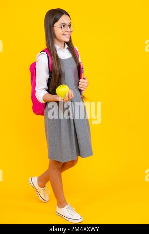 Zurück zur Schule. Teenager Schülerin mit Tasche halten Apfel und Buch, bereit zu lernen. Schulkinder auf isoliertem gelben Hintergrund. Stockfoto