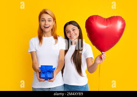 Muttertag. Familie von Mutter und Tochter in legerer Kleidung, zum Feiern, in roter Geschenkbox, isoliert auf gelbem Hintergrund, Studioporträt. Stockfoto