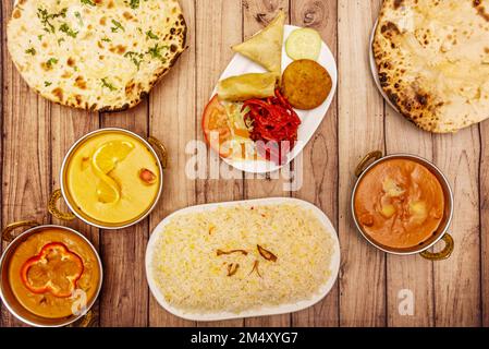 Set aus typischen indischen Gerichten mit Käse-Knoblauch-Naan, Biryani-Reis, verschiedenen süßen und würzigen Currys und Vorspeise Stockfoto