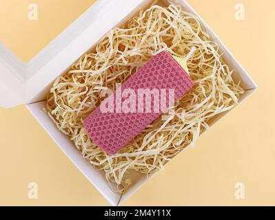 Große handgemachte Kerze aus Naturwachs. Künstlicher Strohhalm für Geschenkverpackungen. Wunderschöne farbige Wachskerze in einer Verpackung, Draufsicht. Na Stockfoto