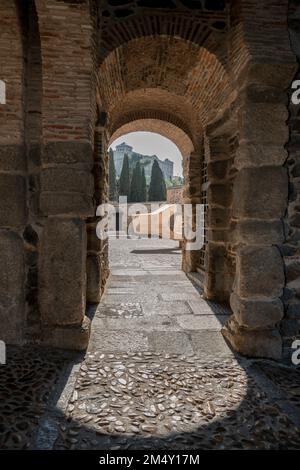 Sonnenstrahlen erleuchten den Kopfsteinpflasterboden eines Steineingangs in der Mauer der monumentalen Stadt Toledo, Spanien Stockfoto