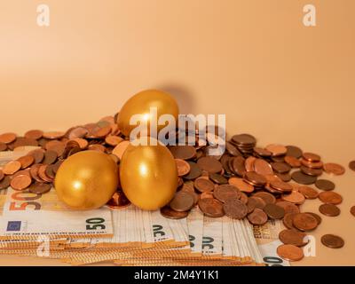 Goldene Eier auf Geld. Goldene Hühnereier auf Euro-Banknoten und -Münzen. Reichtum-Symbol. Einsparungen und Investitionen. Stockfoto