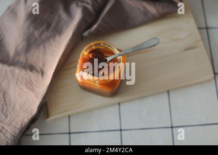 Hausgemachte, gesalzene Karamellsauce im Glas auf einem rustikalen Holztisch. Stockfoto