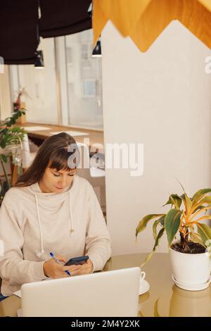 Heimbüro-Frau und Fernarbeit. Eine junge Geschäftsfrau, die an einem Schreibtisch sitzt und ihren Laptop in einem Heimbüro tippt, Stockfoto