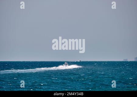 Meereslandschaft mit Wellenoberfläche aus blauem Meerwasser mit weißem Schnellboot, das schnell auf ruhigen Wellen schwimmt. Stockfoto