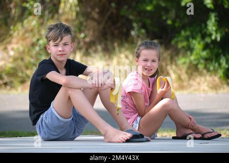 Junge hübsche Teenager Junge und hübsches Mädchen essen leckere reife Banane Naschen im Freien am Sommertag. Stockfoto