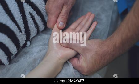 Ein Masseur massiert die Handgelenke eines Mädchens. Stockfoto