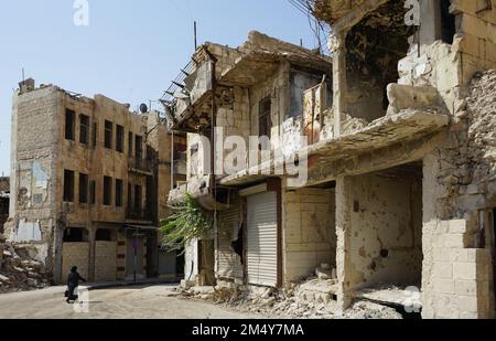 Eine Frau läuft durch ein schwer beschädigtes Viertel in Aleppo. Während des syrischen Bürgerkriegs erlitt die Stadt in den heftigen Schlachten erhebliche Schäden. Syrien Stockfoto