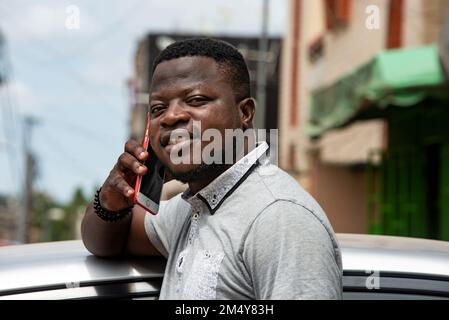 Porträt eines jungen Mannes, der auf der Straße telefoniert und lächelt. Stockfoto