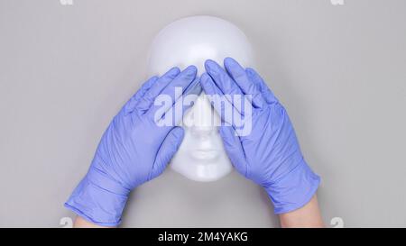 Hände in medizinischen Schutzhandschuhen bedeckte Augen des plastischen Schaufenstergesichts. Medizinische Handschuhe, Maske, Plastikgesicht Stockfoto