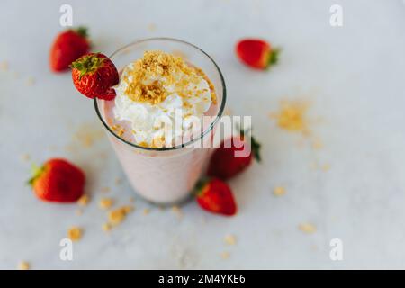 Ein Glas Erdbeermilchshake von oben, umgeben von Erdbeeren mit Sahne Stockfoto