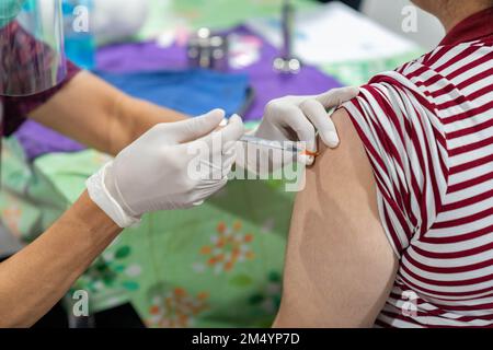 Frau in medizinischer Gesichtsmaske, die Covid-19 oder Grippe-Impfstoff im Krankenhaus erhält. Professionelle Krankenschwester oder Arzt, die dem Patienten eine antivirale Injektion verabreichen Stockfoto