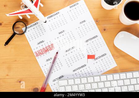 Kalender und Erinnerungen für Geschäftsreisen, Reisen und Urlaub. Gleiter auf dem Schreibtisch mit Flugzeug und Lupe, Stift und Tastatur. Markierung wichtig Stockfoto