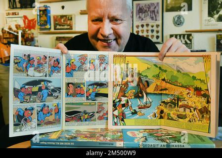 PRODUKTION - 07. Dezember 2022, Sachsen, Leipzig: Sammler Thomas Wilde hält in seiner Wohnung ein Mosaik-Comic mit den Digedags von 1960 und ein Mosaik-Buch mit den Abrafaxen von 1976 in den Händen. (l-r). Sie gehören etwa 8000 Mosaikgegenständen, die der 63-jährige ehemalige Engländer- und Deutsche Lehrer gesammelt hat. In seiner Wohnung gibt es wahrscheinlich wirklich alles, was das 'Mosaik' zu bieten hat. Neben Broschüren und Büchern gibt es unter anderem viele Figuren, Auslagen, Becher, T-Shirts, Spielzeuge, Zuckerkonen, Videos und Puzzles (für Papa 'Mr. Wilde fehlt nichts - 'Mo Stockfoto