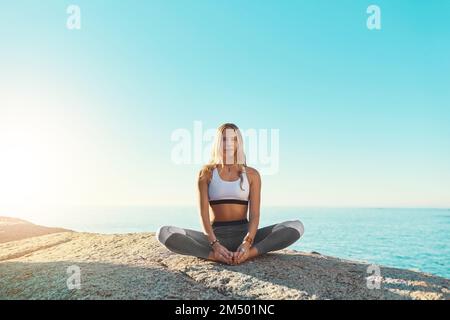 Yoga ist der Grund, warum ich ein glücklicheres Leben führe. Eine junge Frau, die am Strand Yoga macht. Stockfoto